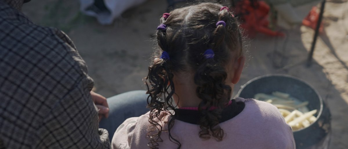 Una niña observa como un miembro de su familia cocina fuera de su tienda de campaña en el sur de Gaza.